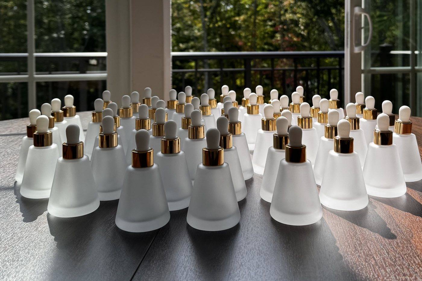 The Edition One bottles on a table by a window: frosted glass, gold collars, white dropper bulbs