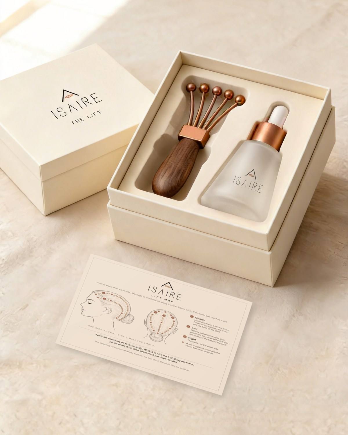 The open Maison Isaire kit: the cleansing oil in frosted glass with a satin copper collar and a white dropper bulb, the walnut tool with five tines, the Lift Map card, and the lid with the mark and THE LIFT